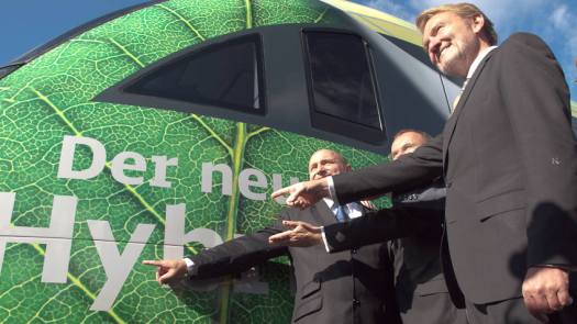 Drei Männer zeigen auf einen Schriftzug