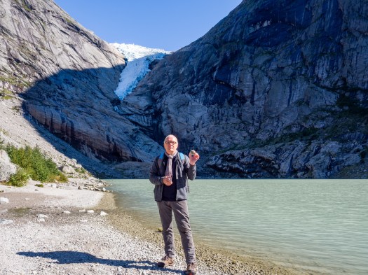 Mann steht an einem See mit Gletscher