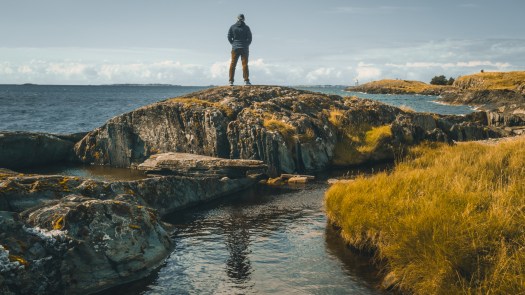 Mann steht auf Felsen und schaut aufs Meer