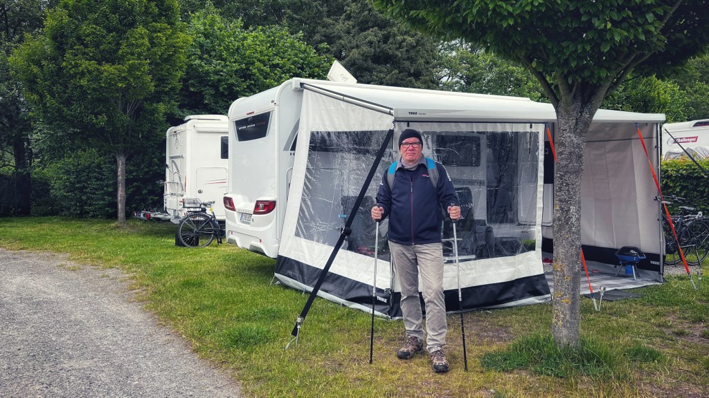 Ein Mann steht vor Wohnmobilzelt mit Wanderstöcken