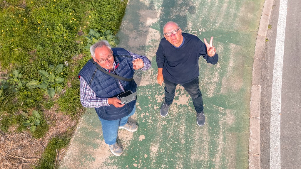 Zwei Männer aus Drohnensicht, einer hält doe Steuerung, der andere zeigt das Peacezeichen