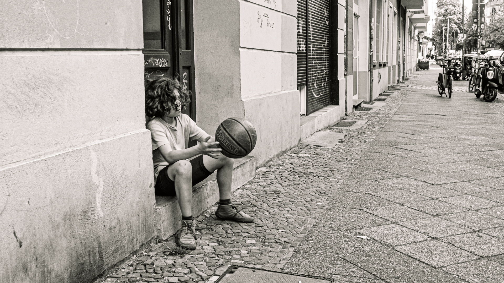 Junge sitzt an Haustür in Berlin und hält einen Ball