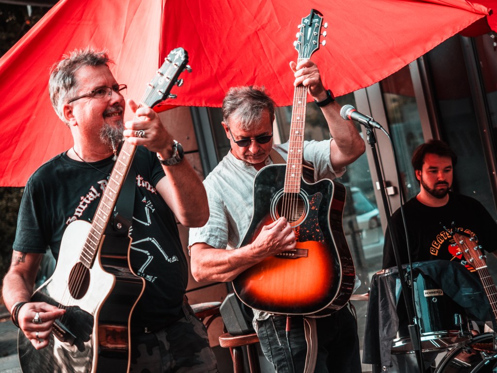 Zwei Musiker mit Gitarren, im Hintergrund ein Schlagzeuger