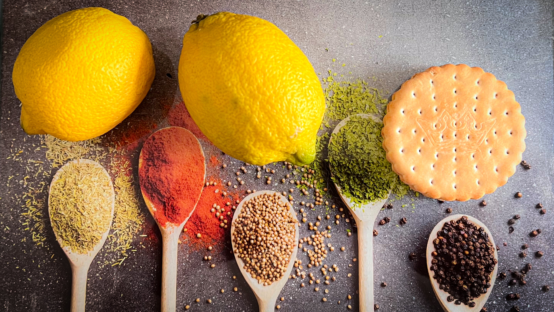 Ein Küchenbrett mit Bildern von Gewürzlöffeln. Auf dem Brett liegen 2 Zitronen und ein Keks