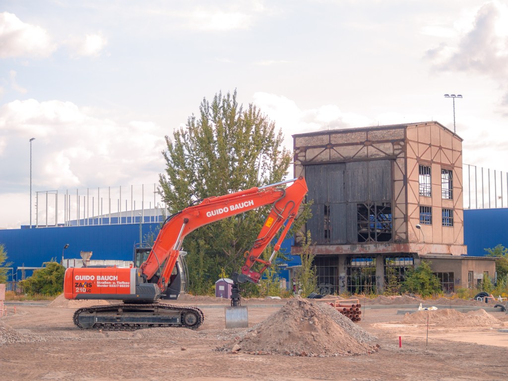 Ein Bagger auf einem Baugelände, ein altes Fabrikgebäude im Hintergrund