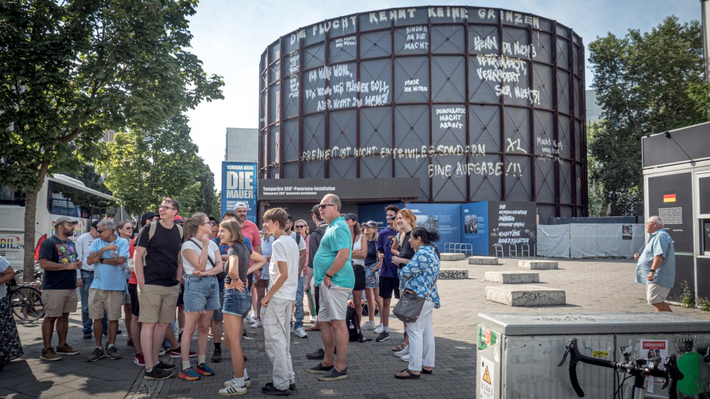 Besuchergruppe vor dem Mauer-Panorama am Checkpoint Charlie in Berlin
