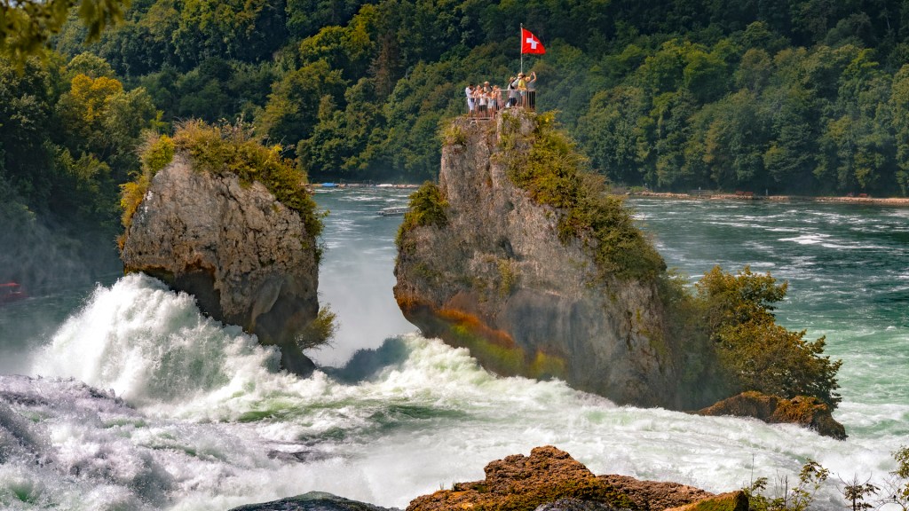 Felsen im Rheinfall mit Touristen und Schweizer Flagge