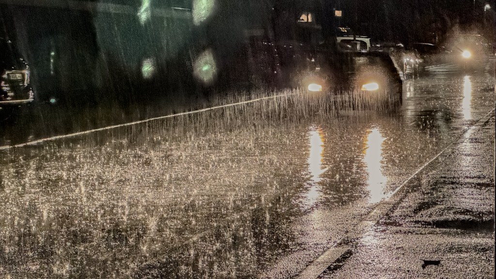 Regen glitzert im Gegenlicht eines Autos im dunklen auf einer Straße