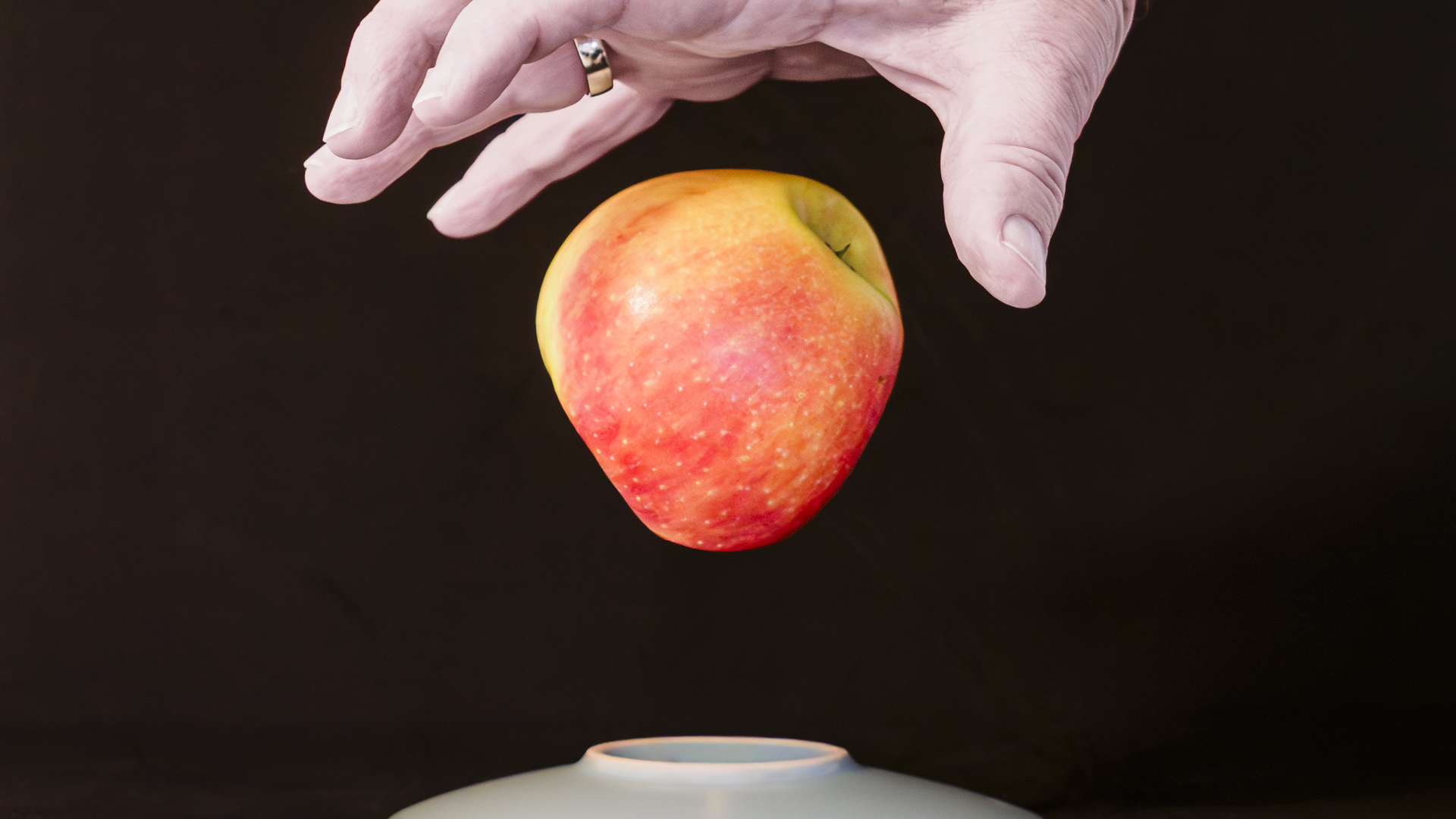 Ein roter Apfel schwebt zwischen Untertasse und einer Hand