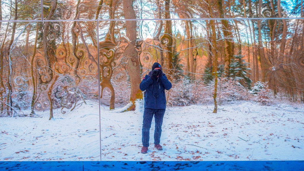 Ein Kubus mit spiegelnder Oberfläche in einem winterlichen Wald zeigt den Fotograf