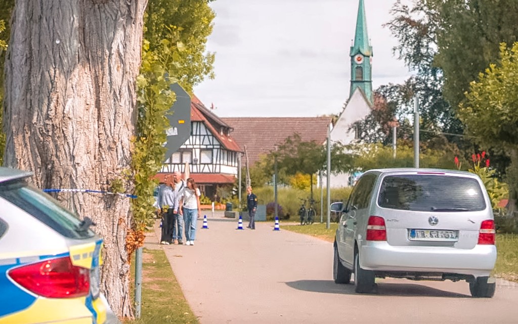 Ein silbernes Auto fährt eine Straße entlang, im Hintergrund Gebäude