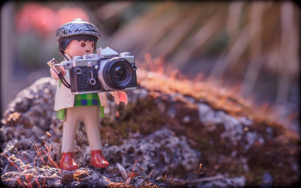 Eine Playmobilfigur mit einem Modell einer Olympuskamera vor sich