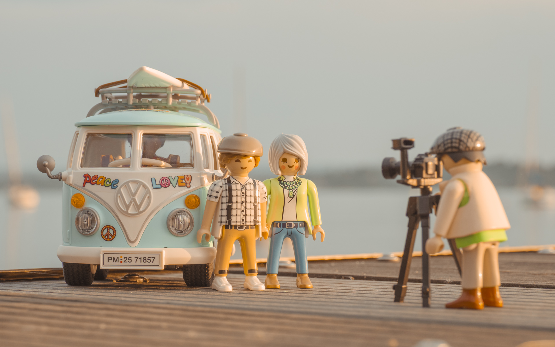 Ein Playmobil VW Bus T1, dafür stehen 2 Figuren. Eine weitere Figur mit einer Kamera fotgrafiert die beiden Anderen