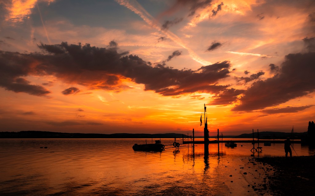 Hinter einer Anlegestelle am Bodensee glüht der Abendhimmel in roten Farben.