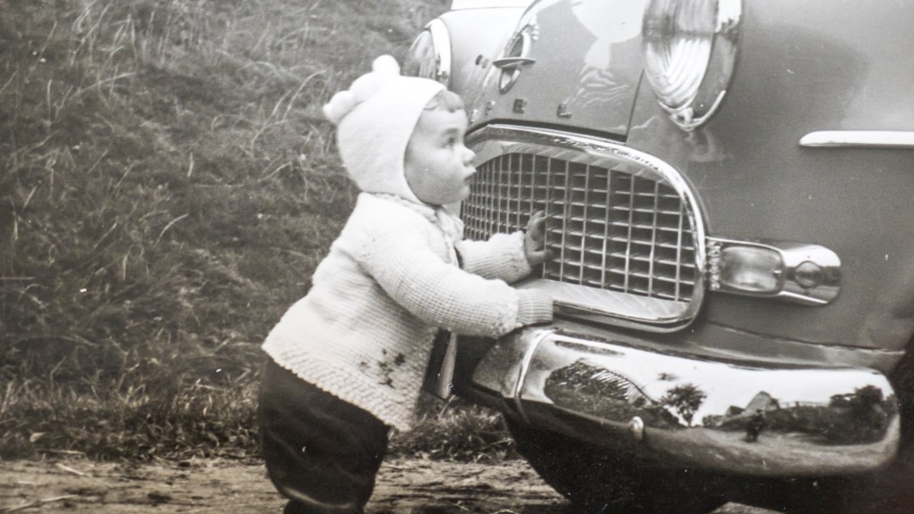 Ein schwarz-weiss Foto mit einem kleinen Jungen, der vor einem alten Opel steht, vermutlich Ende der 50er Jahre